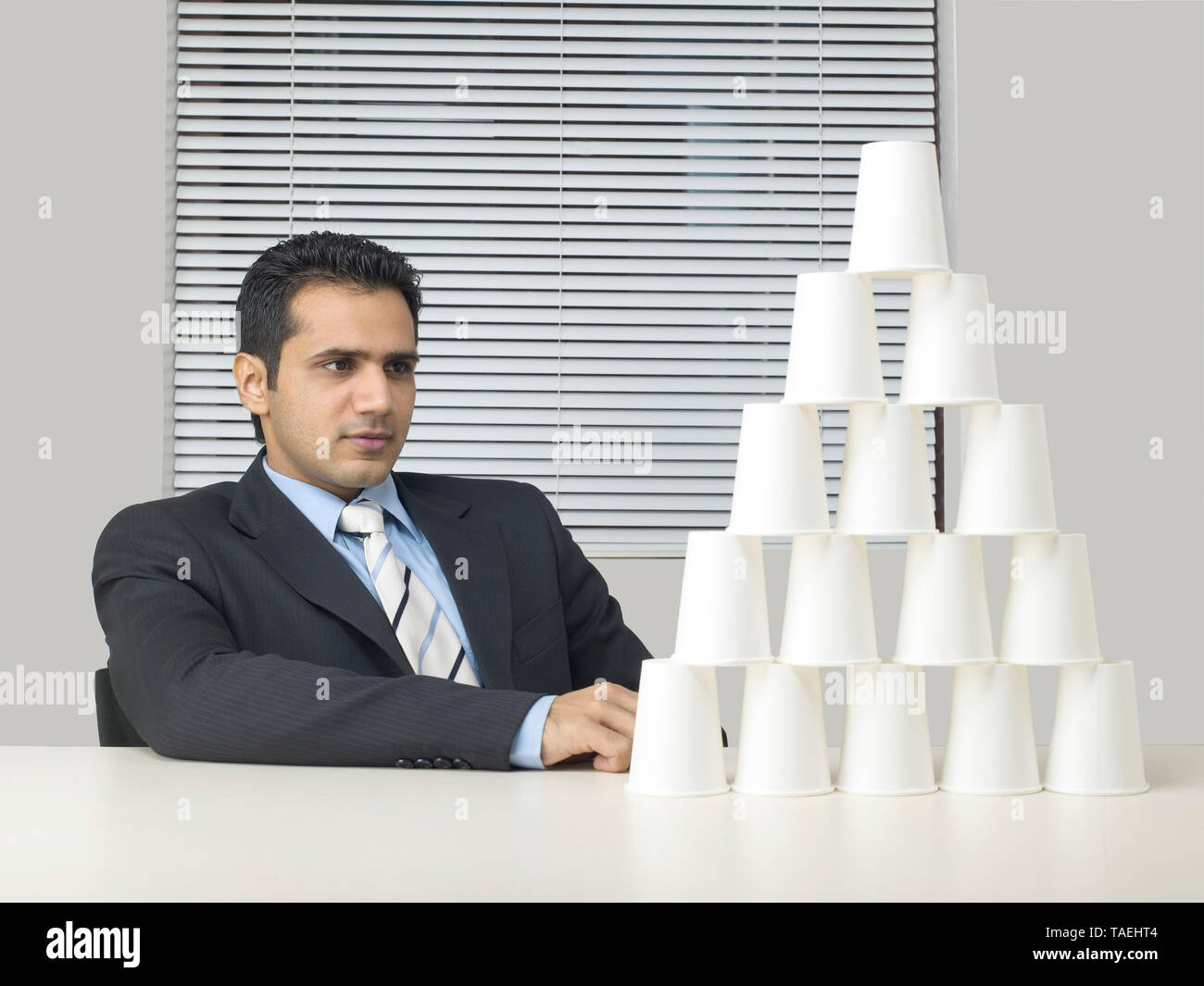 CORPORATE EXECUTIVE IN A SUIT MAKING A BUILDING FROM PAPER CUPS Stock ...