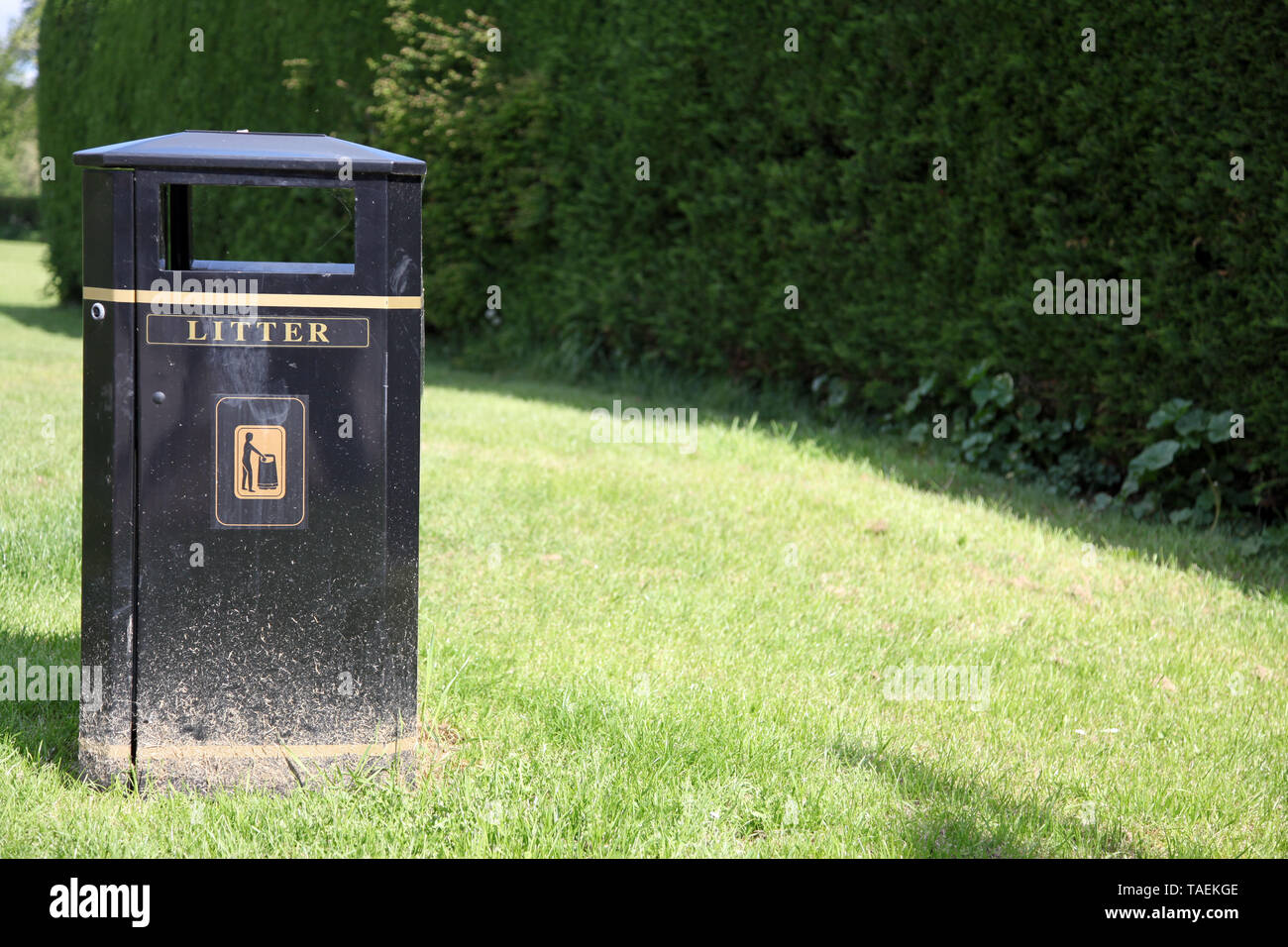 Black council litter bin on left set against green field with copy space to right Stock Photo