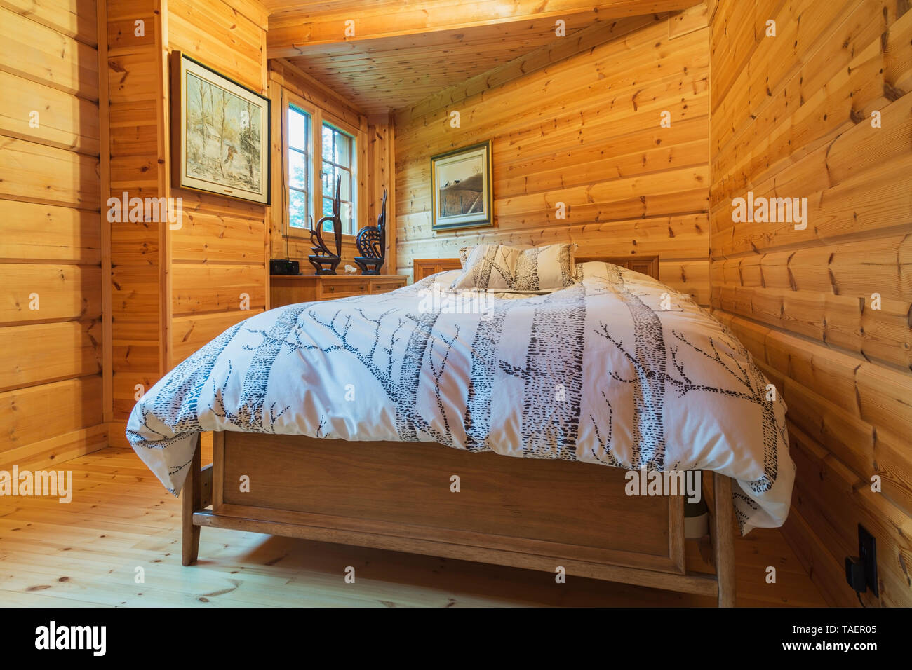 Queen size bed with wood frame and striped bedspread and matching pillows in long and narrow bedroom inside a piece sur piece Scots pine log home, Quebec, Canada. This image is property released. CUPR0334 Stock Photo