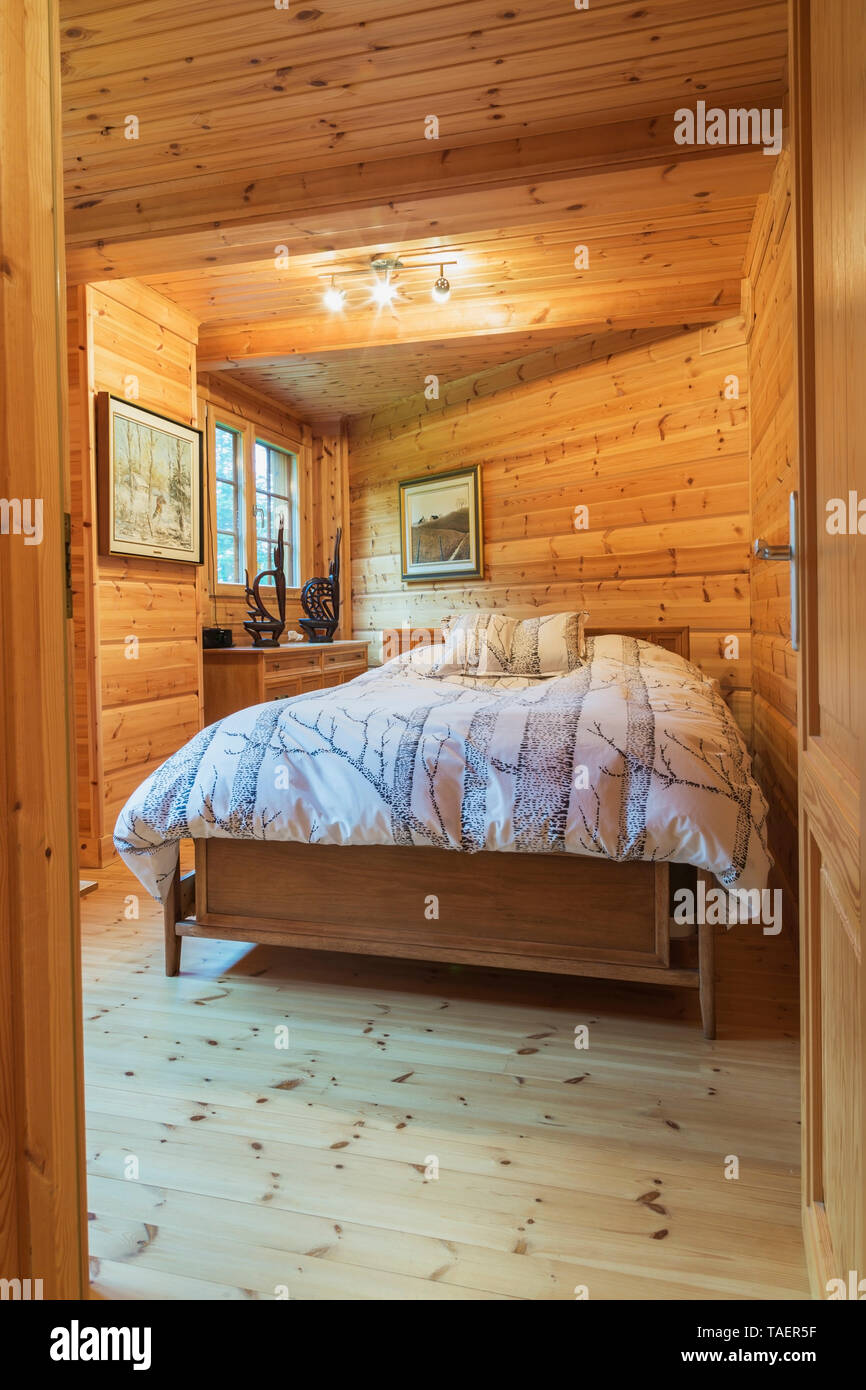 Queen size bed with wood frame and striped bedspread and matching pillows in long and narrow bedroom inside a piece sur piece Scots pine log home, Quebec, Canada. This image is property released. CUPR0334 Stock Photo