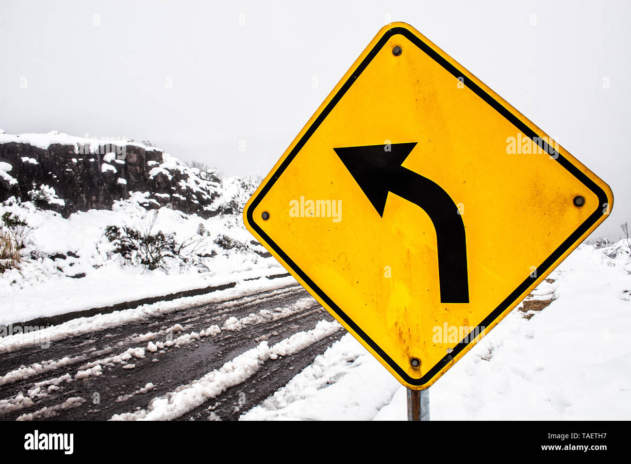 Left curve warning sign on the road that leads to Morro da Igreja surrounded by snow.  Urubici, Santa Catarina, Brazil. Stock Photo