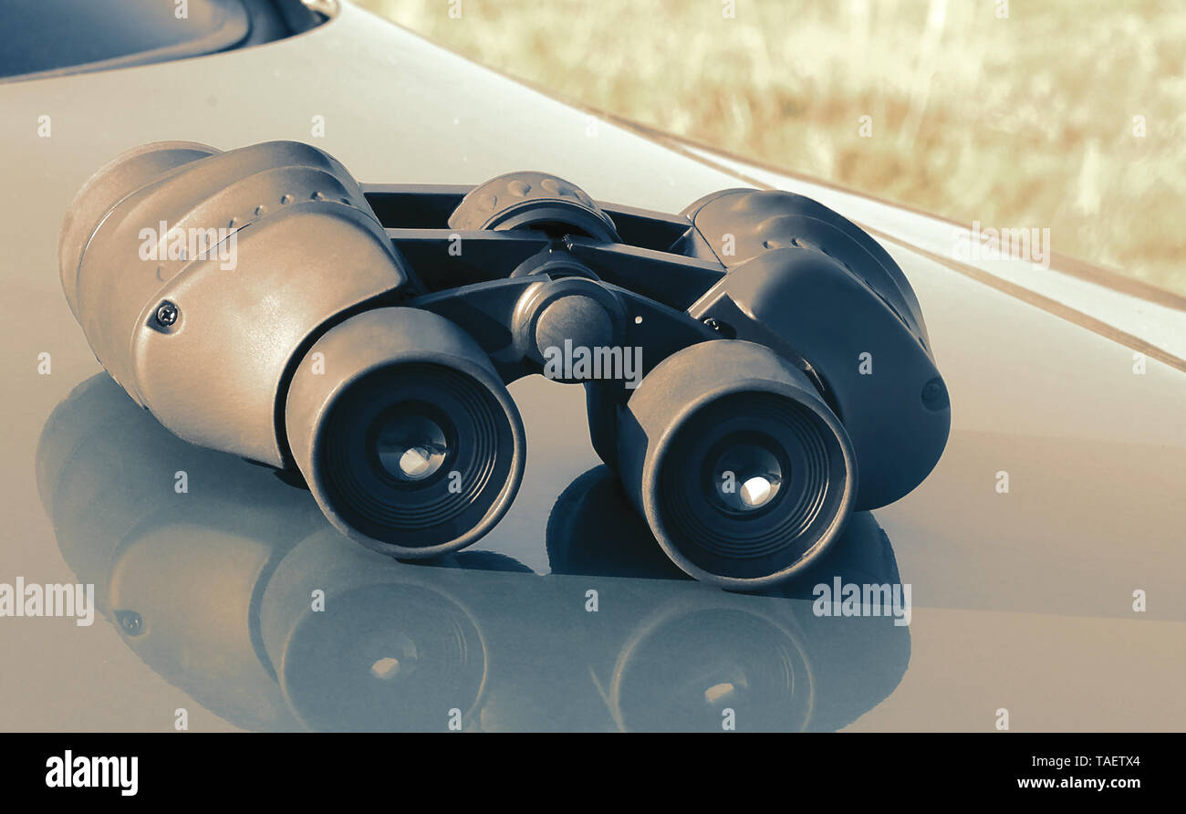 On the hood of a blue car is the binoculars. Stock Photo