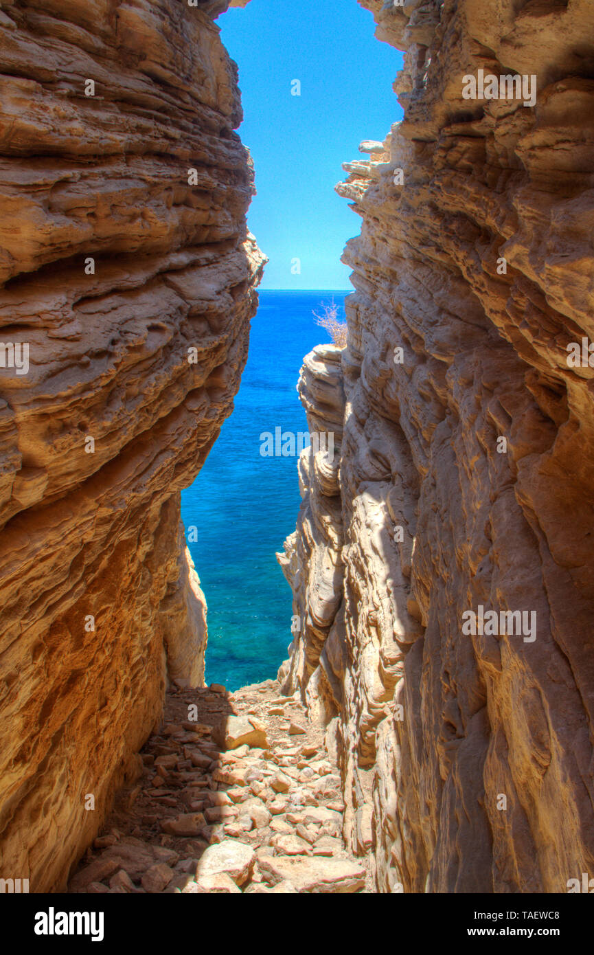 View through a narrow cave at the blue sea and sky Stock Photo