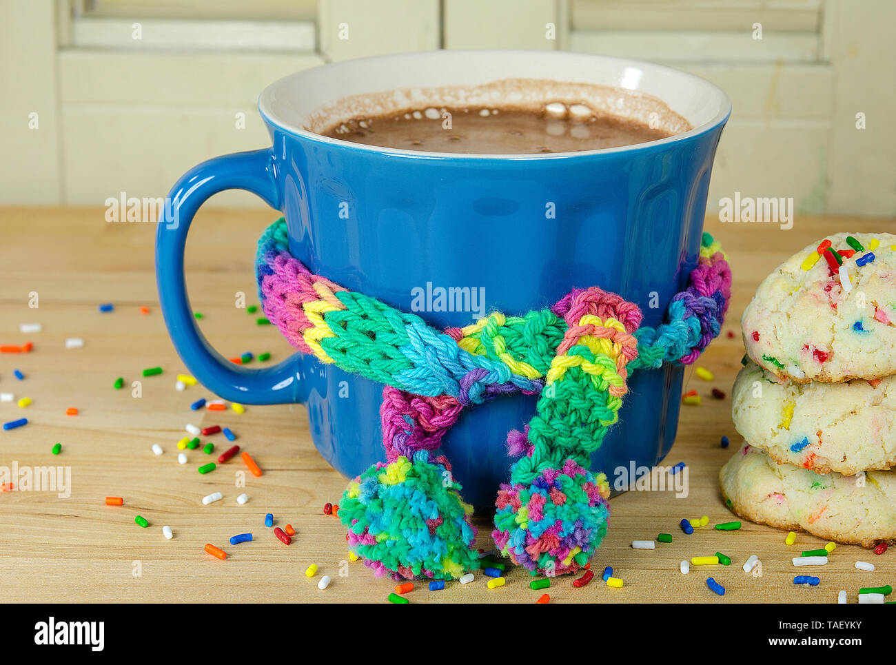 cookies and hot chocolate drink with knit scarf tied around blue mug on wood table and sprinkles Stock Photo