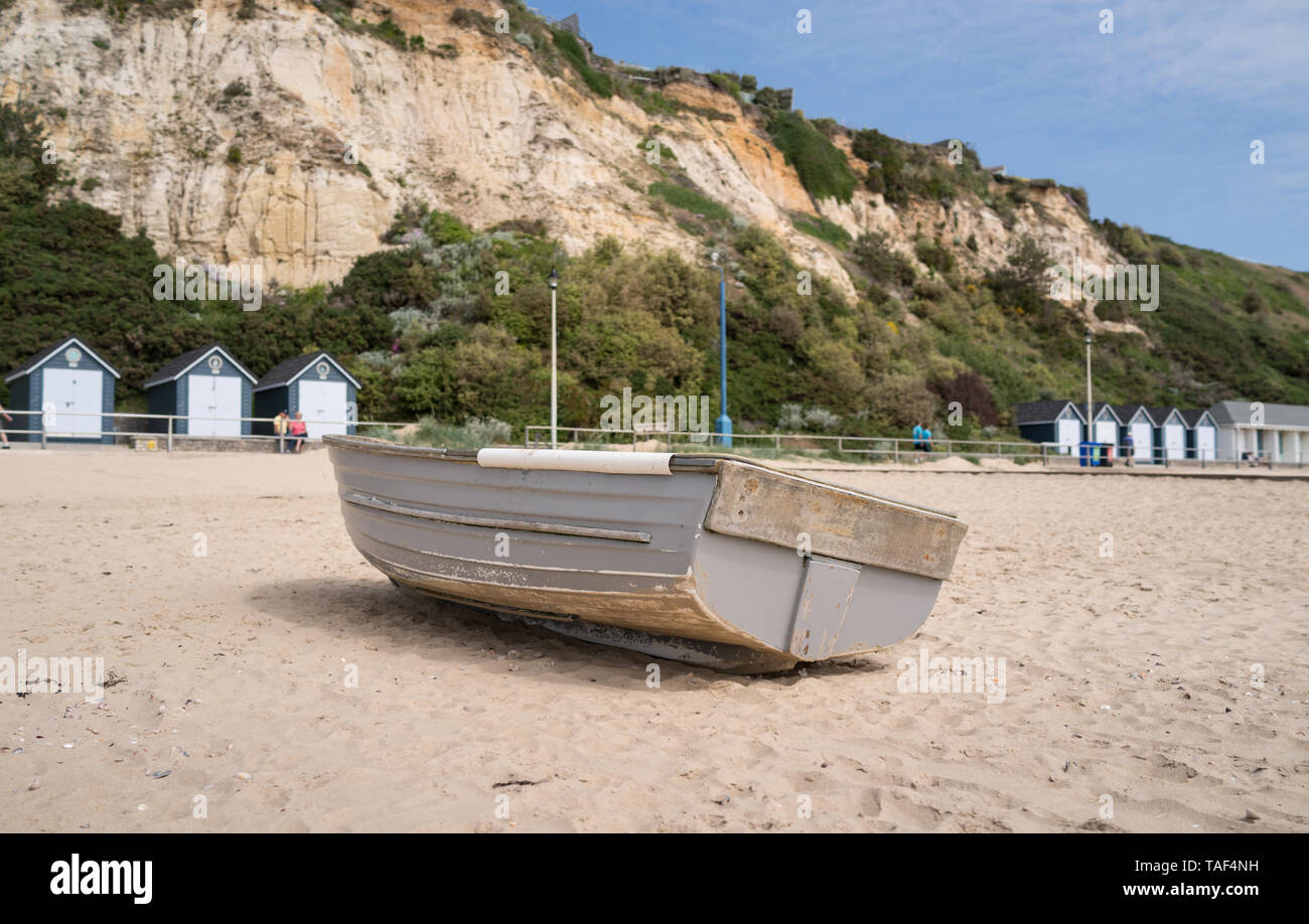 Old fishing rowing boat on Bournemouth beach with cliffs and beach huts in background near Branksome Chine Stock Photo