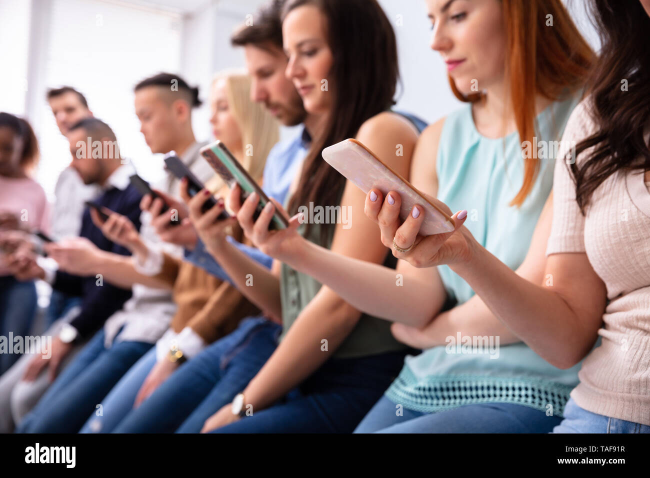 Multi-ethnic Young People Leaning Near Table In Row Using Smartphone Stock Photo