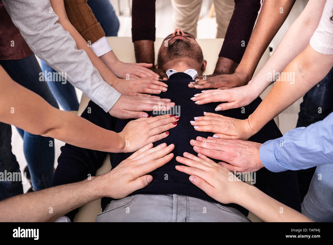 Group Of Hands Touching Man's Body Lying On Table During Reiki Session Stock Photo