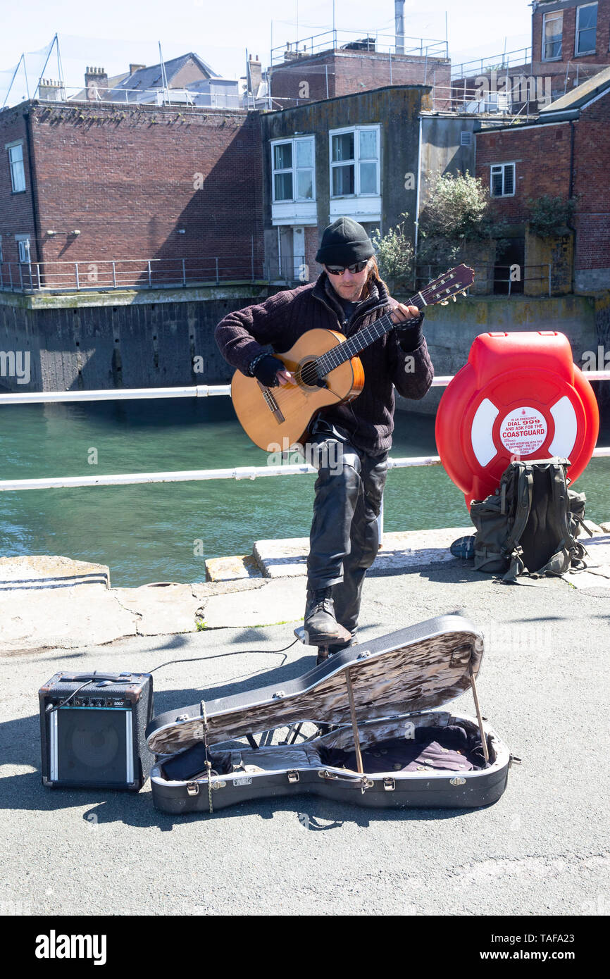 Guitar playing busker dressed against the elements on the Prince of Wales pier in Falmouth, Cornwall U.K. Stock Photo