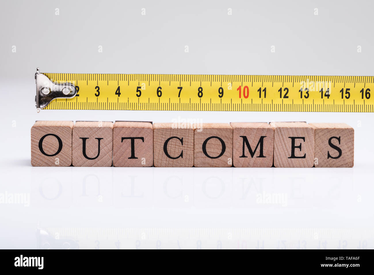 Measurement Of Outcomes Word On Wooden Blocks Using Measuring Tape Stock Photo