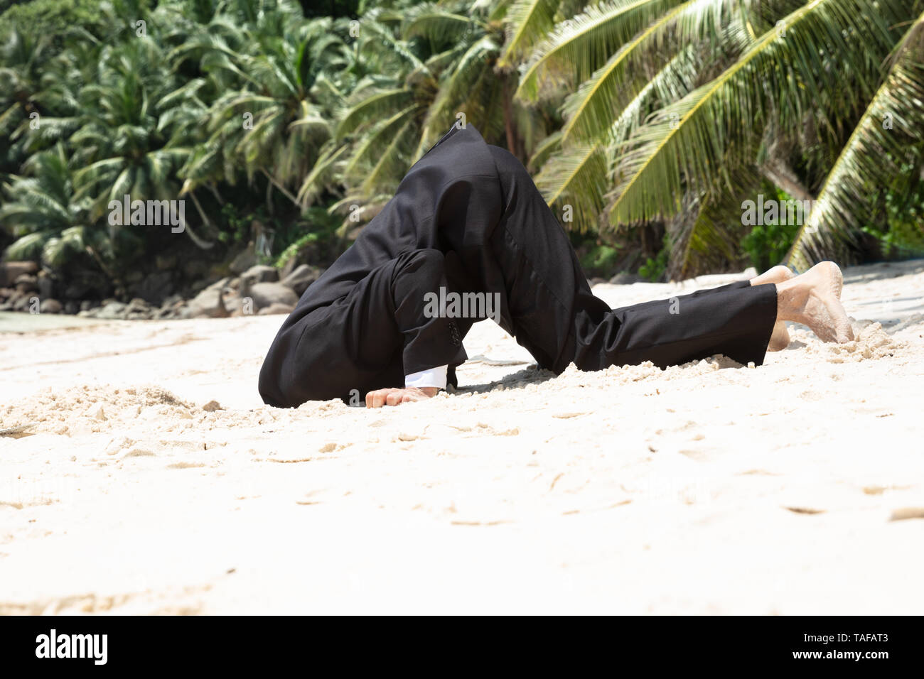 Side View Of Unsuccessful Businessman Burying His Head In The Sand At Beach Stock Photo