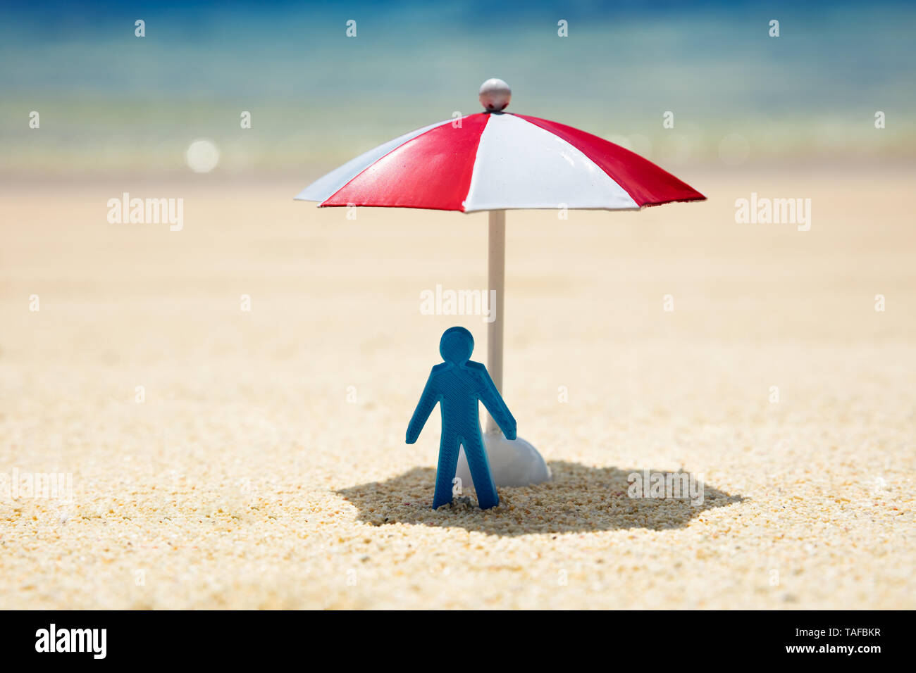 Close-up Of A Blue Human Figure Standing Under The Red And White Umbrella On Beach Stock Photo