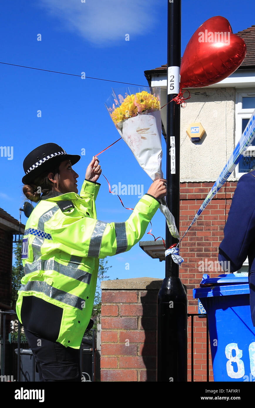 A police officer takes flowers from school children to lay at a property on Gregg House Road in