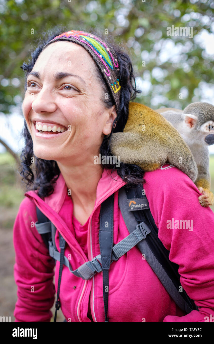 Tourist having a great time with a cute squirrel monkey on her shoulder at an animal shelter on the riverbank of the Amazon River near Iquitos, Peru Stock Photo