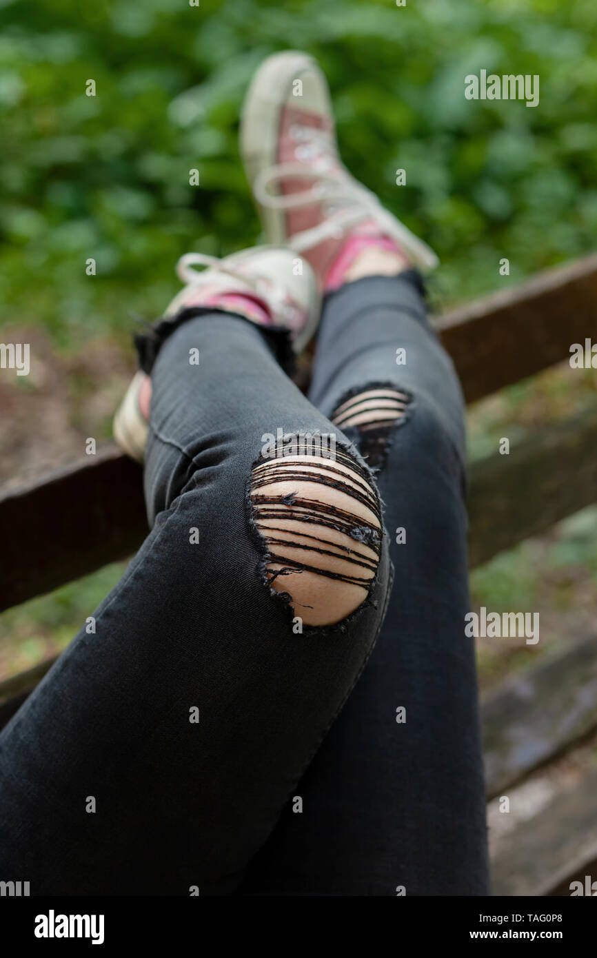 Female legs in black ripped jeans and pink canvas sneakers casually