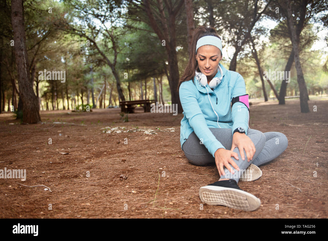 Runner girl with ankle injury holds foot to reduce pain after running. Problem for athlete training outdoors Stock Photo