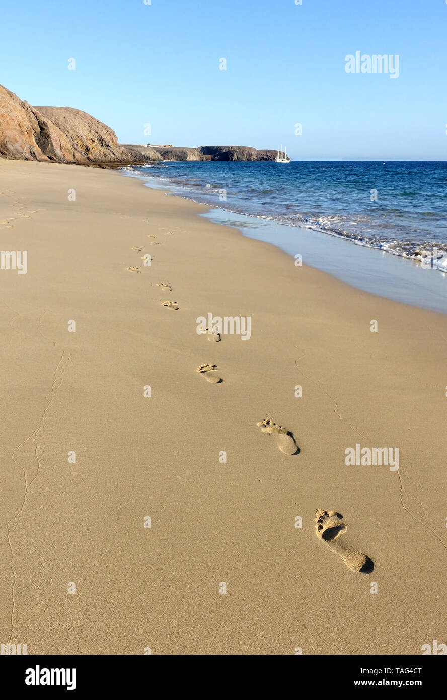 A trail of adult foot prints are left on the shore in the golden sand on Papagayo beach, Lanzarote. The beach is bathed in warm evening sunshine Stock Photo