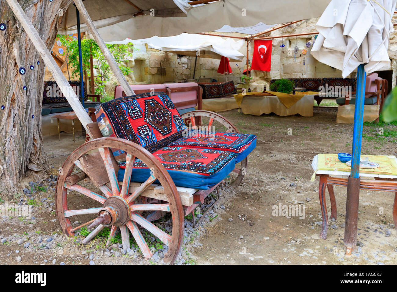 An old wooden cart on large wheels is fitted as a soft chair at a table under the tent in the old courtyard of a Turkish house. Stock Photo