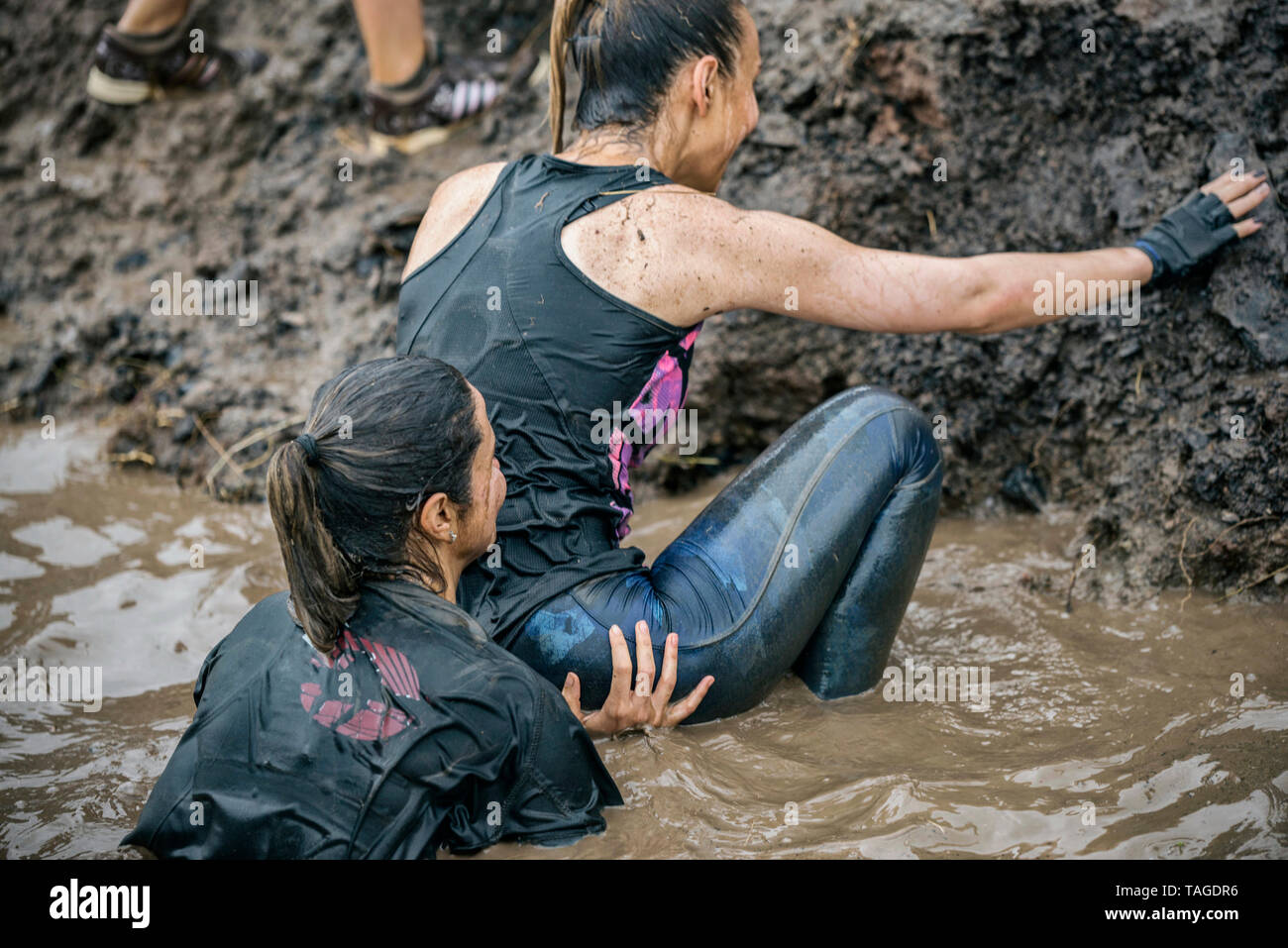 SOFIA, BULGARIA - JULY 7 2018:  a girl is supporting her partner from behind in order to climb over a muddy obstacle in a strength race Stock Photo