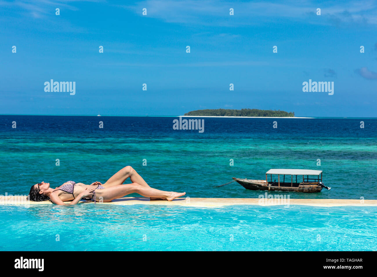 one caucasian woman enjoying vacations  sunbathing on a infinity swimming pool by the seaside looking at the idian ocean Muyuni  in Unguja aka Zanzibar Island Tanzania East Africa Stock Photo