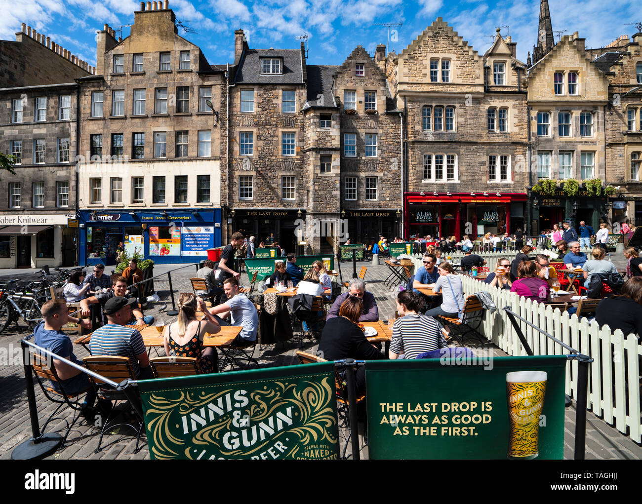 Many people drinking in bars outdoors in warm weather at Grassmarket in