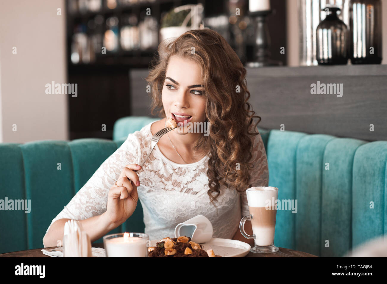 Beautiful blonde woman 20-24 year eating brownie dessert and drinking coffee in cafe. Looking away. Stock Photo