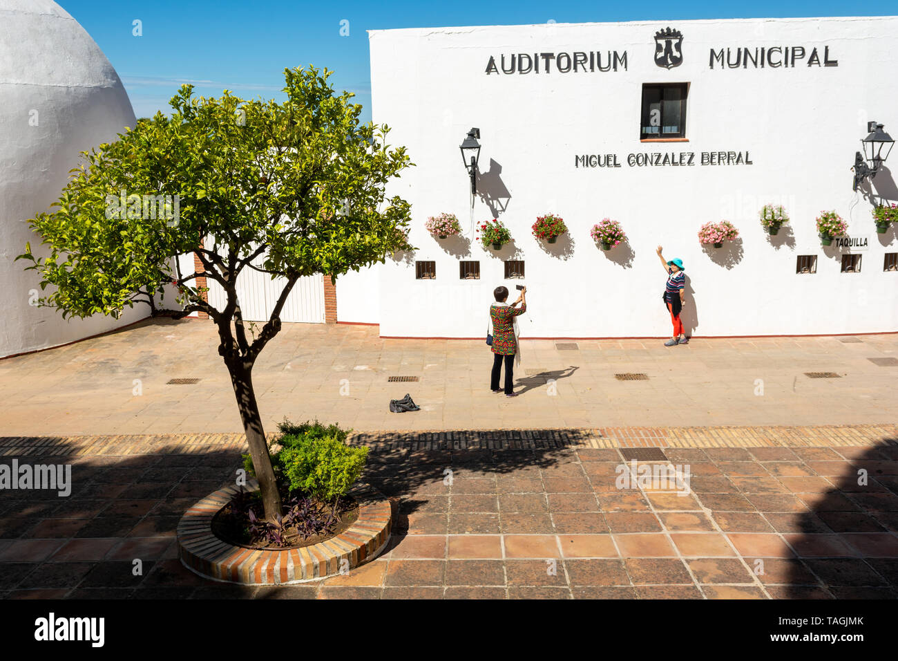 Tourists taking photographs outside the white walled building of the Municipal Auditorium in the mountain village of Mijas, Andalusia region, Spain Stock Photo