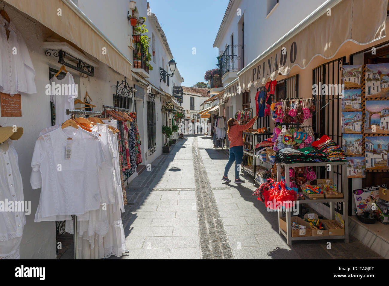 Shopkeeper hanging up clothes outside a shop in a narrow street in Mijas, Andalusia region, Spain Stock Photo