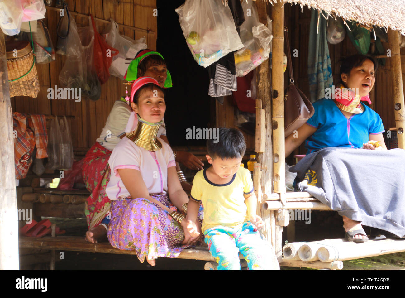 LONGNECK KAREN VILLAGE, THAILAND - DECEMBER 17. 2017: Long neck family sitting in front of a bamboo hut Stock Photo