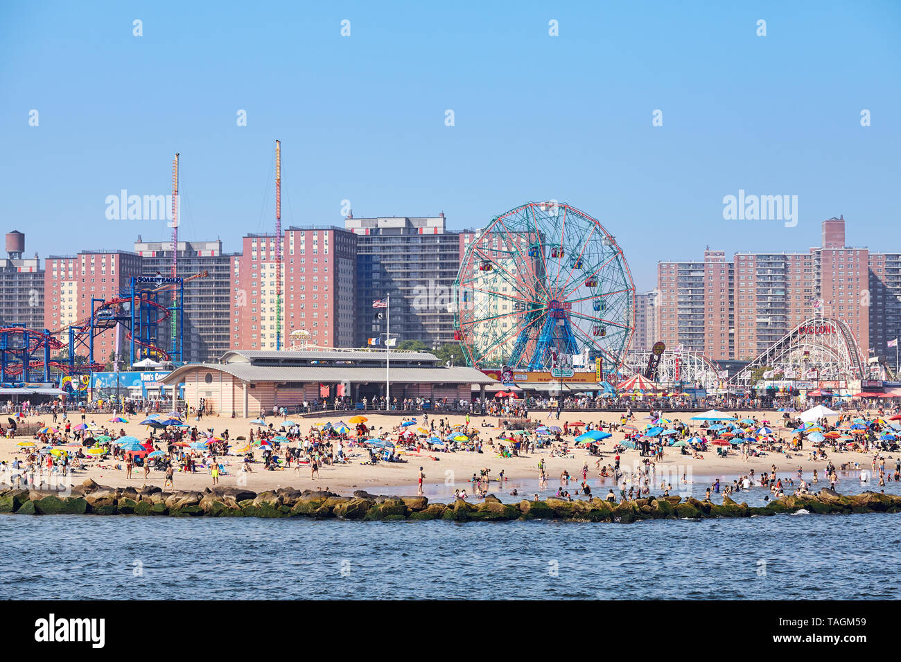 New York, USA - July 02, 2018: Crowded Coney Island beach and amusement parks seen from the pier on a sunny day. Stock Photo