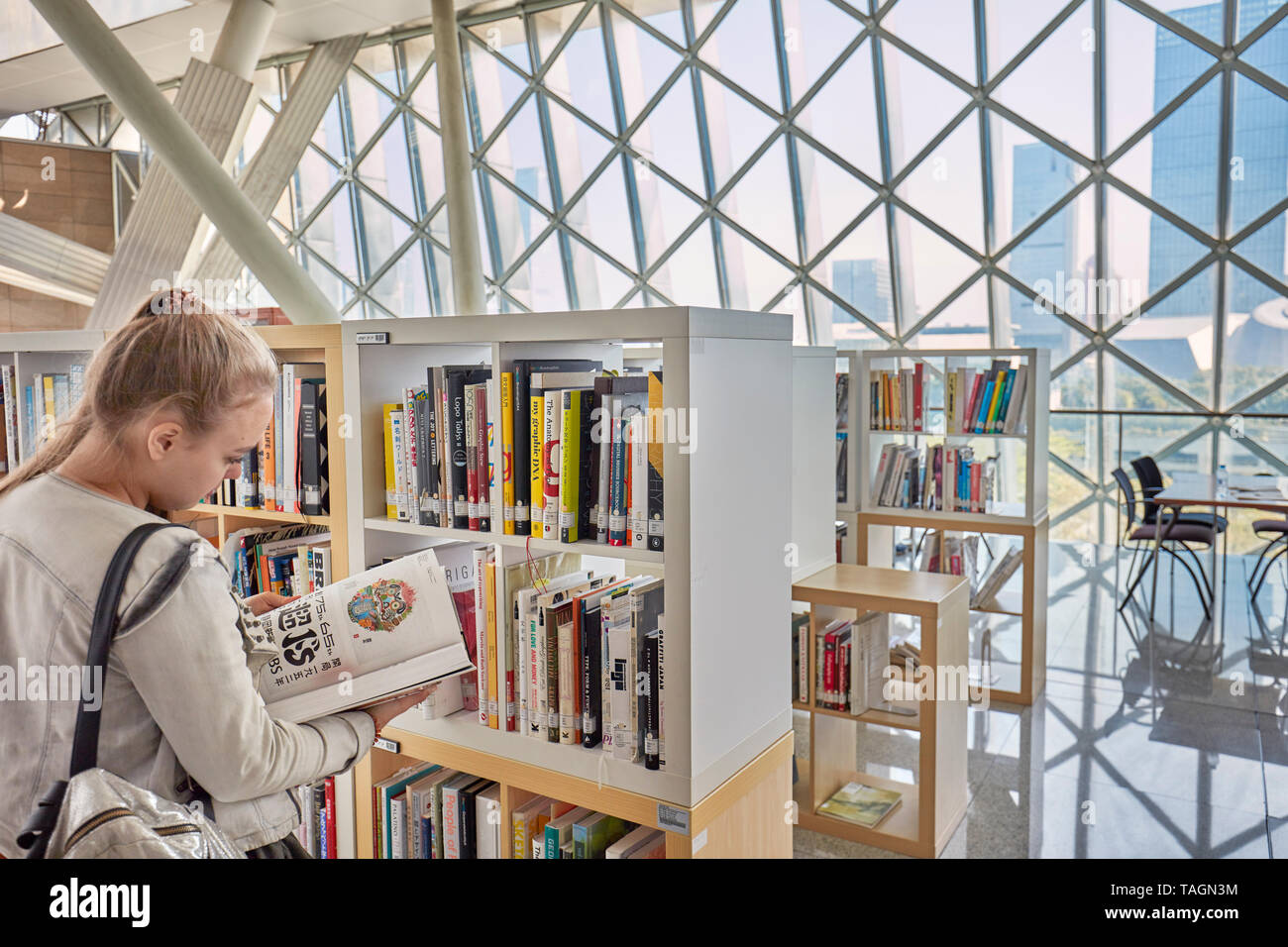 Young Caucasian girl reads a book in Shenzhen Library at Shenzhen Cultural Center. Shenzhen, Guangdong Province, China. Stock Photo