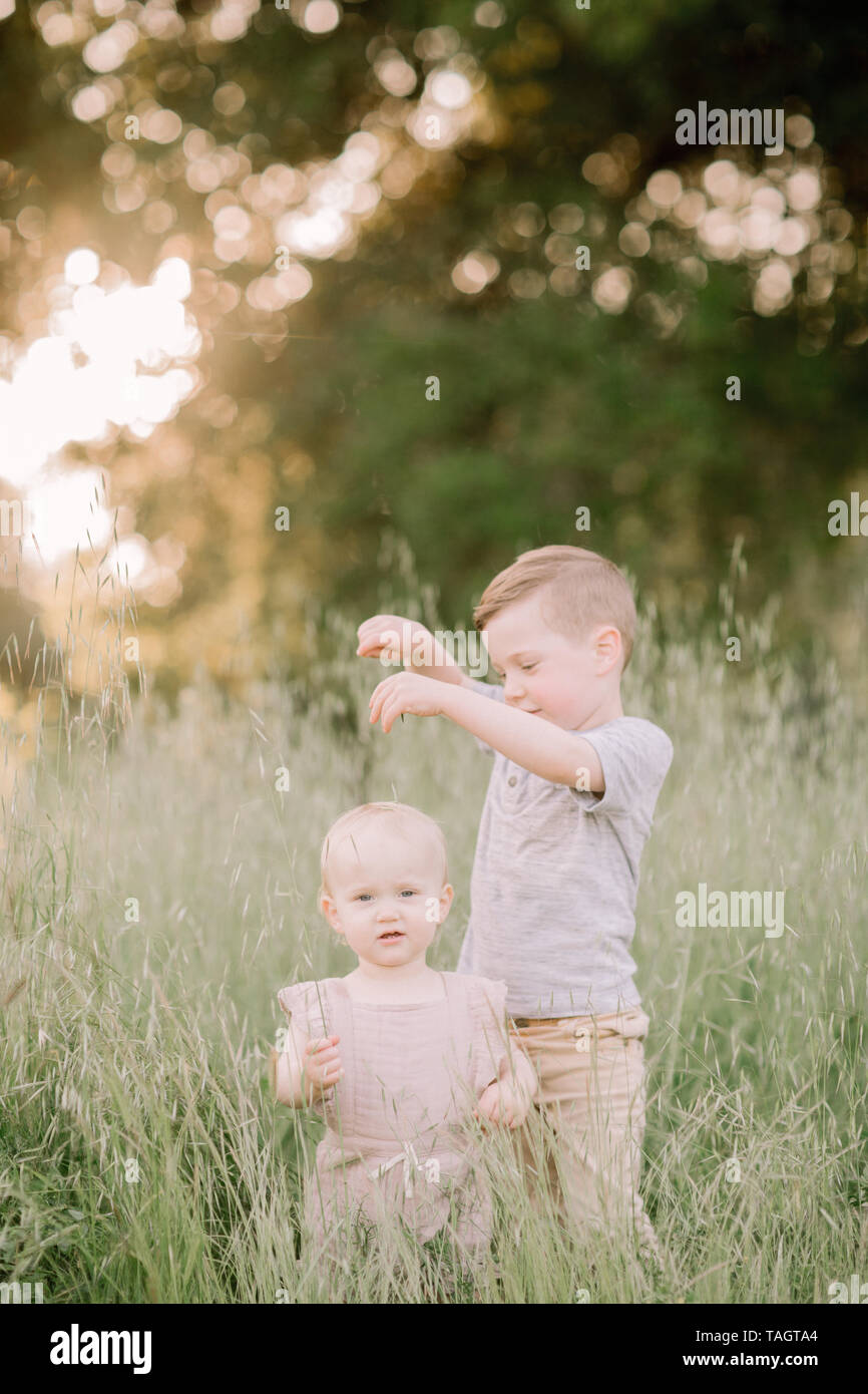 Big brother and baby sister standing in field outside Stock Photo