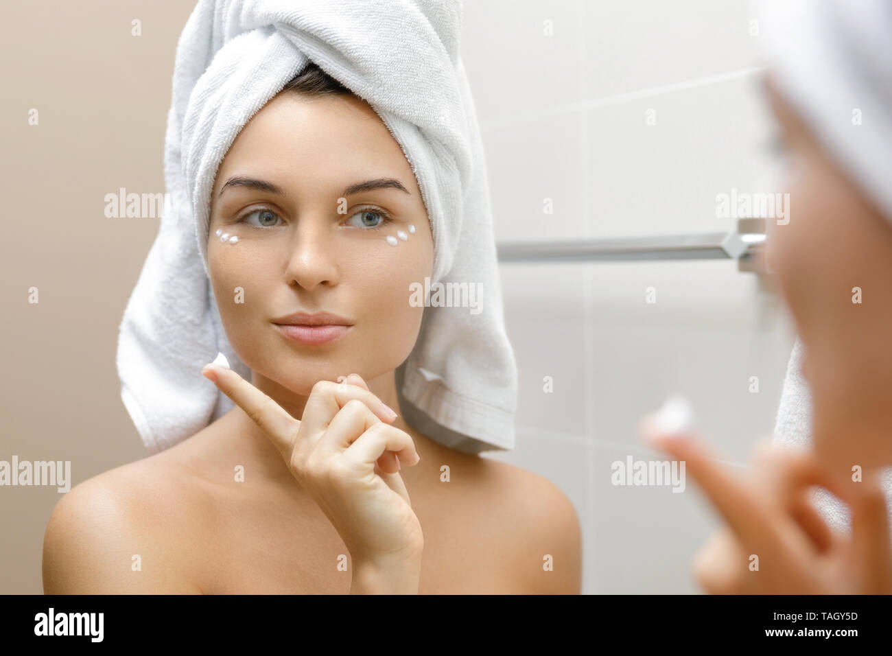 Woman in bathroom is applying moisturizing and anti-aging cream under her eyes Stock Photo