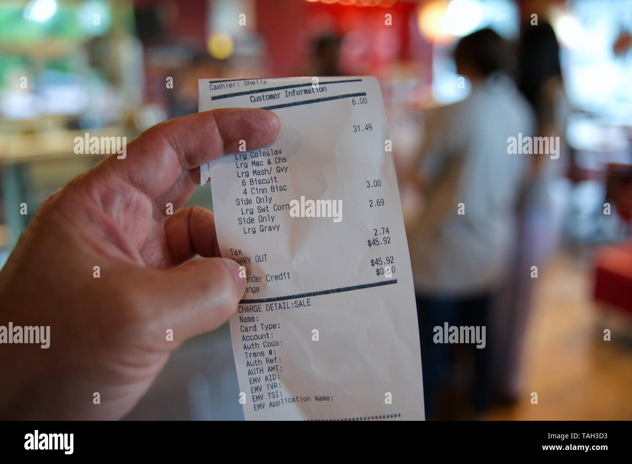 Checking the restaurant receipt for accuracy with young women customers in the background picking up their take out food. Stock Photo