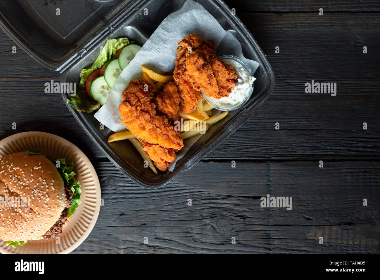 Hamburger, french fries and fried chicken in takeaway containers on the wooden background. Food delivery and fast food concept Stock Photo