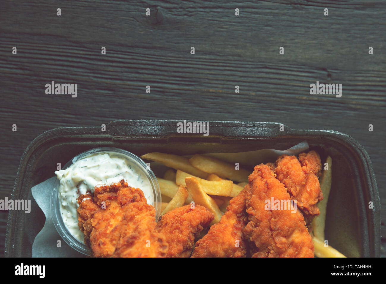 Fried chicken and french fries and in a takeaway container on the wooden background. Food delivery and fast food concept Stock Photo