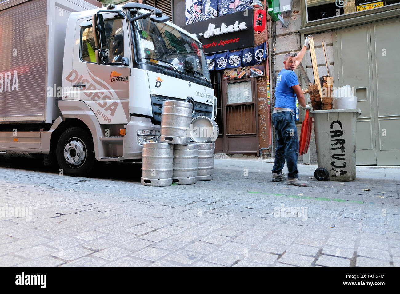 Man taking out a trash bin in front of a stack of empty beer kegs on the street in front of a beer delivery truck in Madrid, Spain. Stock Photo