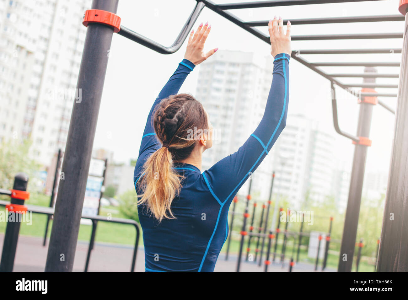 Attractive fit young woman in sport wear girl pulls up on bar at street