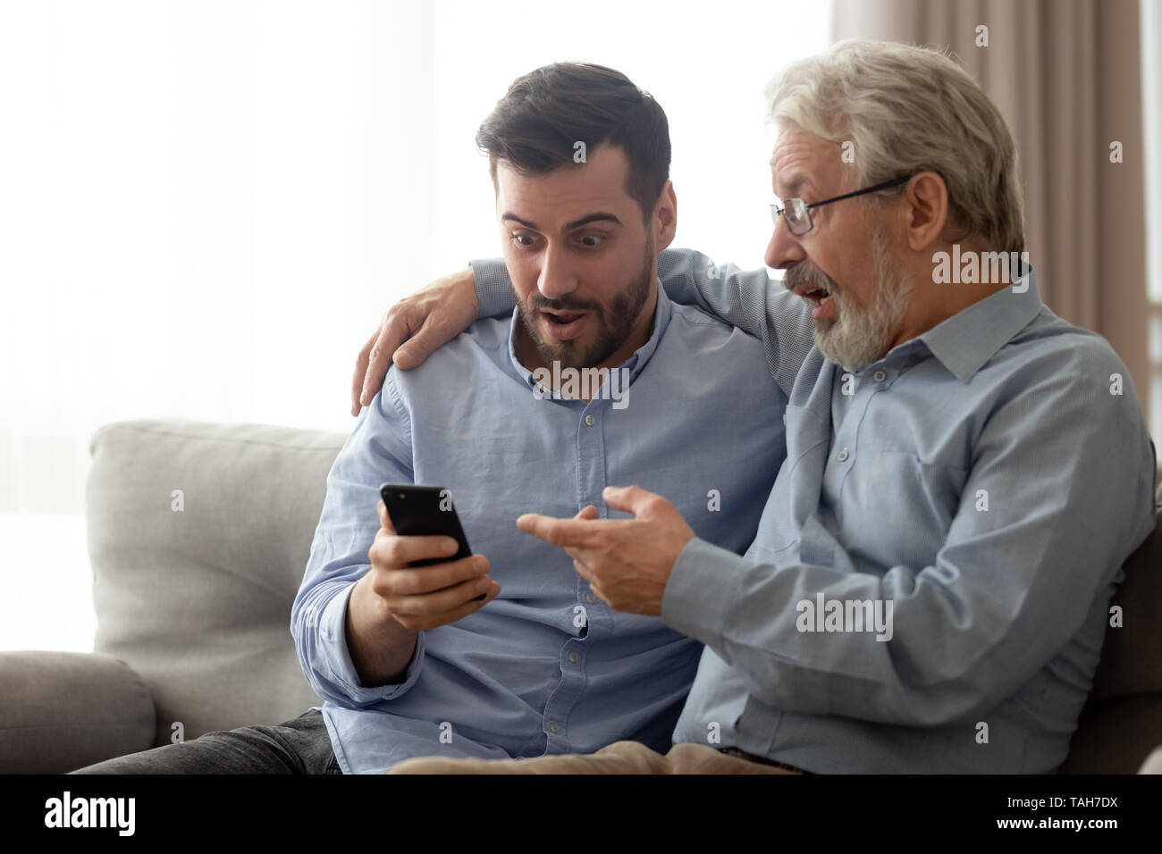 Young man with senior father shocked reading news on smartphone Stock Photo