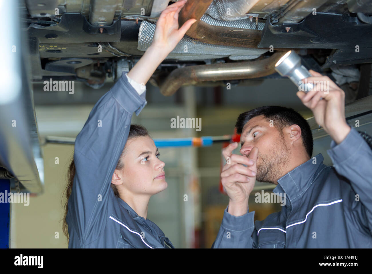 male and female mechanics working underneath car together Stock Photo