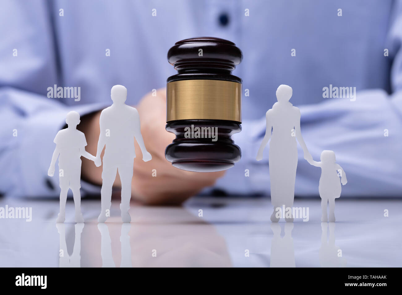 Close-up Of A Judge Striking Gavel Between Family Figure Cut Out Over Reflective Desk Stock Photo