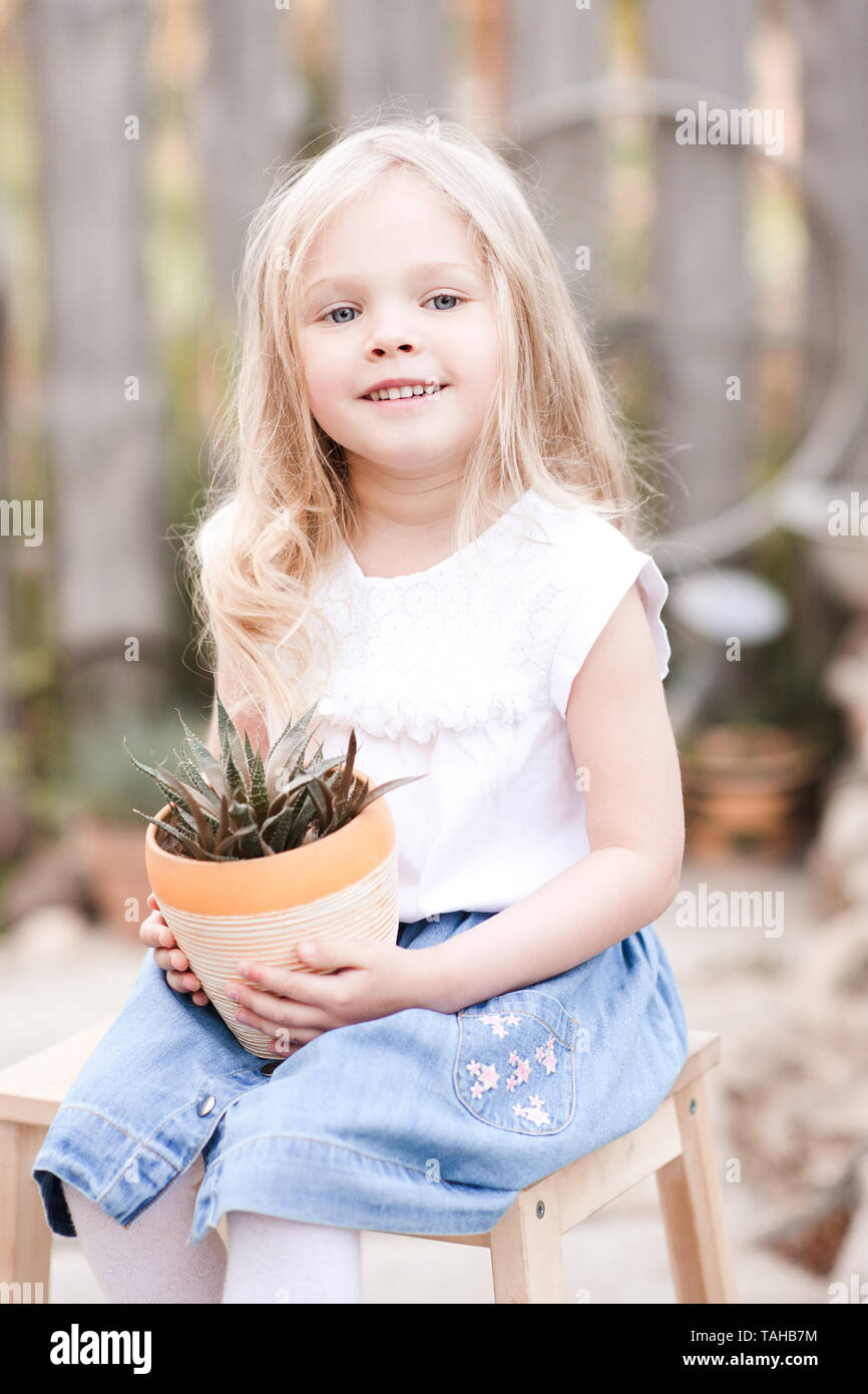 Smiling kid girl holding flower in pot outdoors. Looking at camera ...