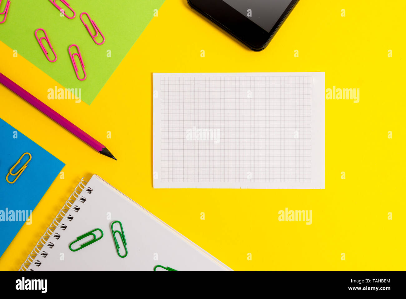 Paper sheets squared notebook pencil clips smartphone colored background Stock Photo