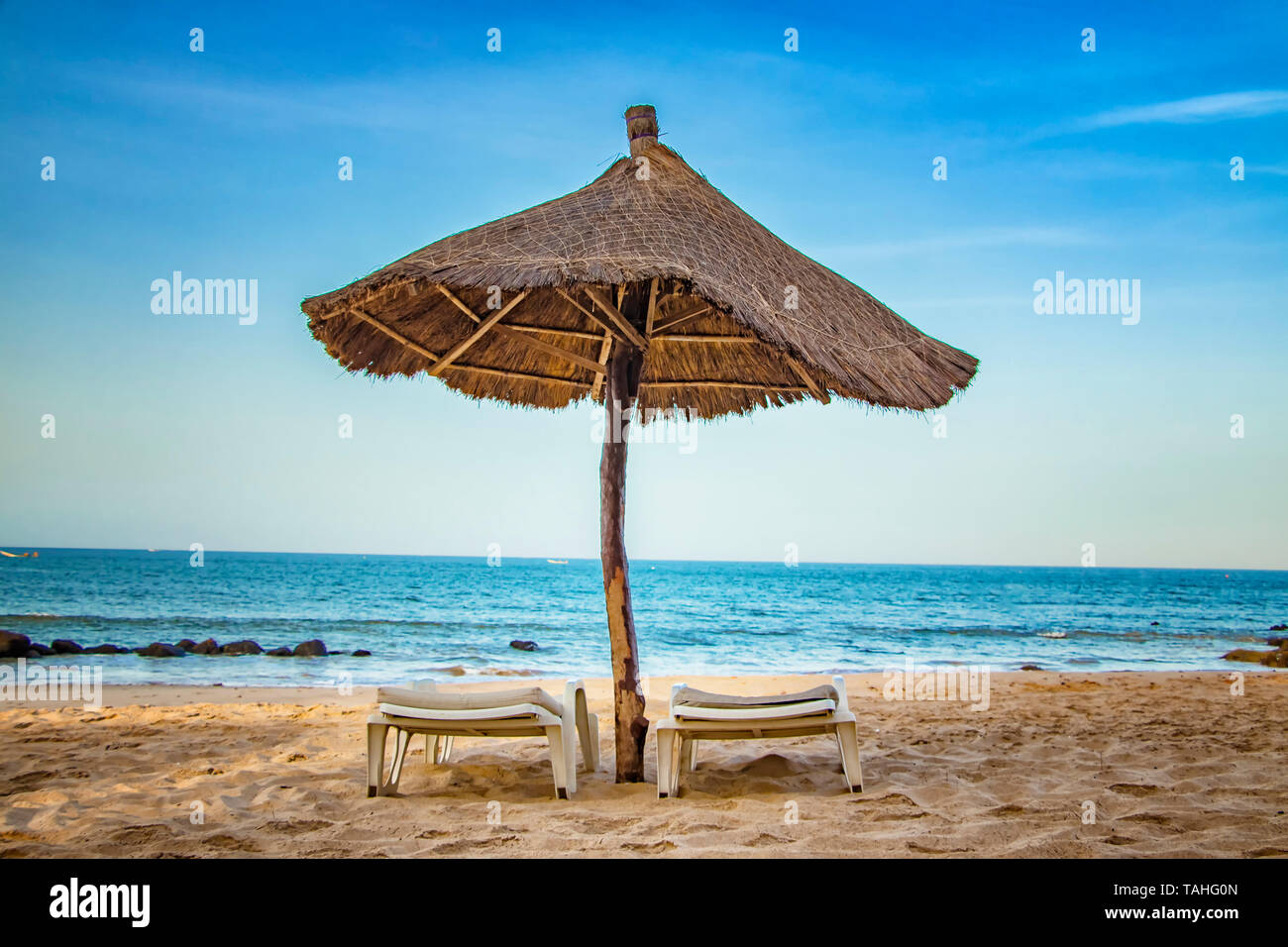 Pair of sunbed with parasol on beautiful empty beach near clear sea. It is a tropical paradise in Africa, Senegal. There is blue sky. It is the right  Stock Photo