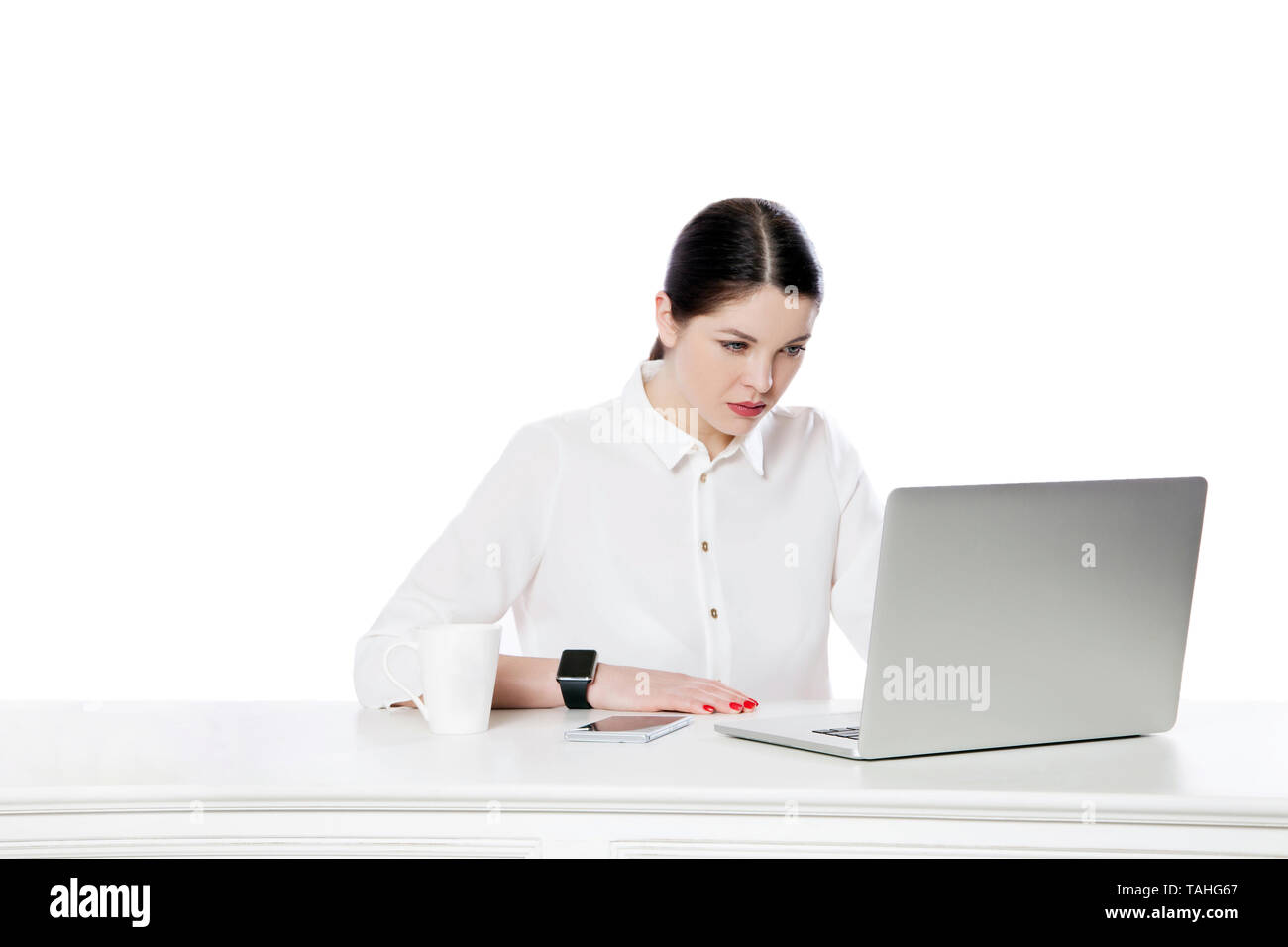 Portrait of attentive serious attractive brunette businesswoman in white shirt sitting with laptop and looking at display and reading something. indoo Stock Photo