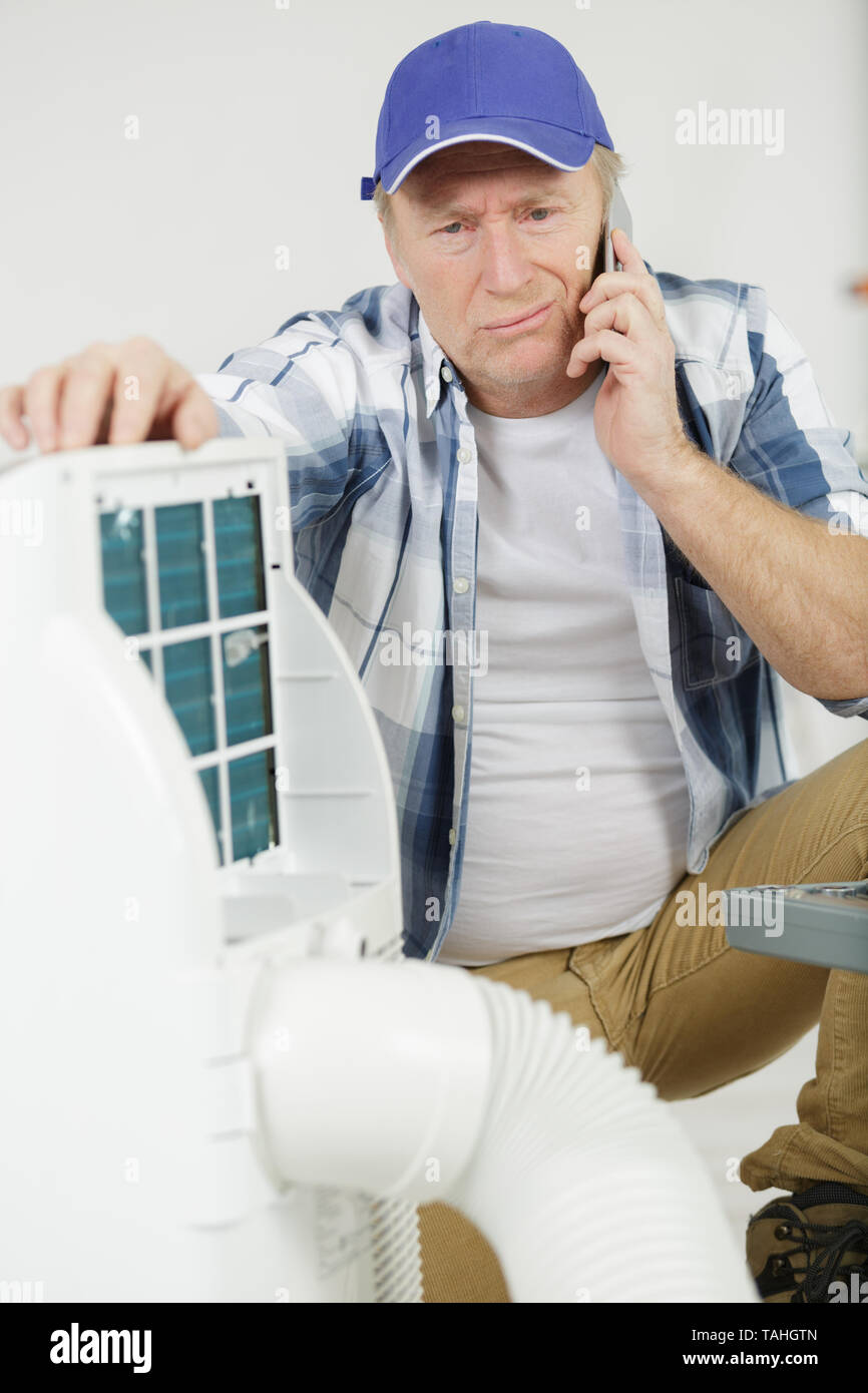 mature handyman on the phone repairing air conditioning system Stock