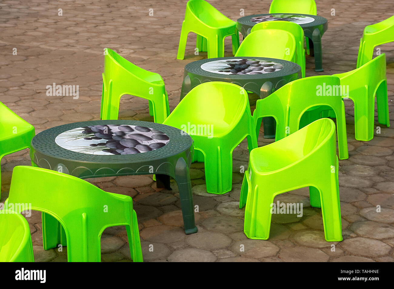 Empty low seat plastic chairs and tables in bright green on the pavement. Stock Photo