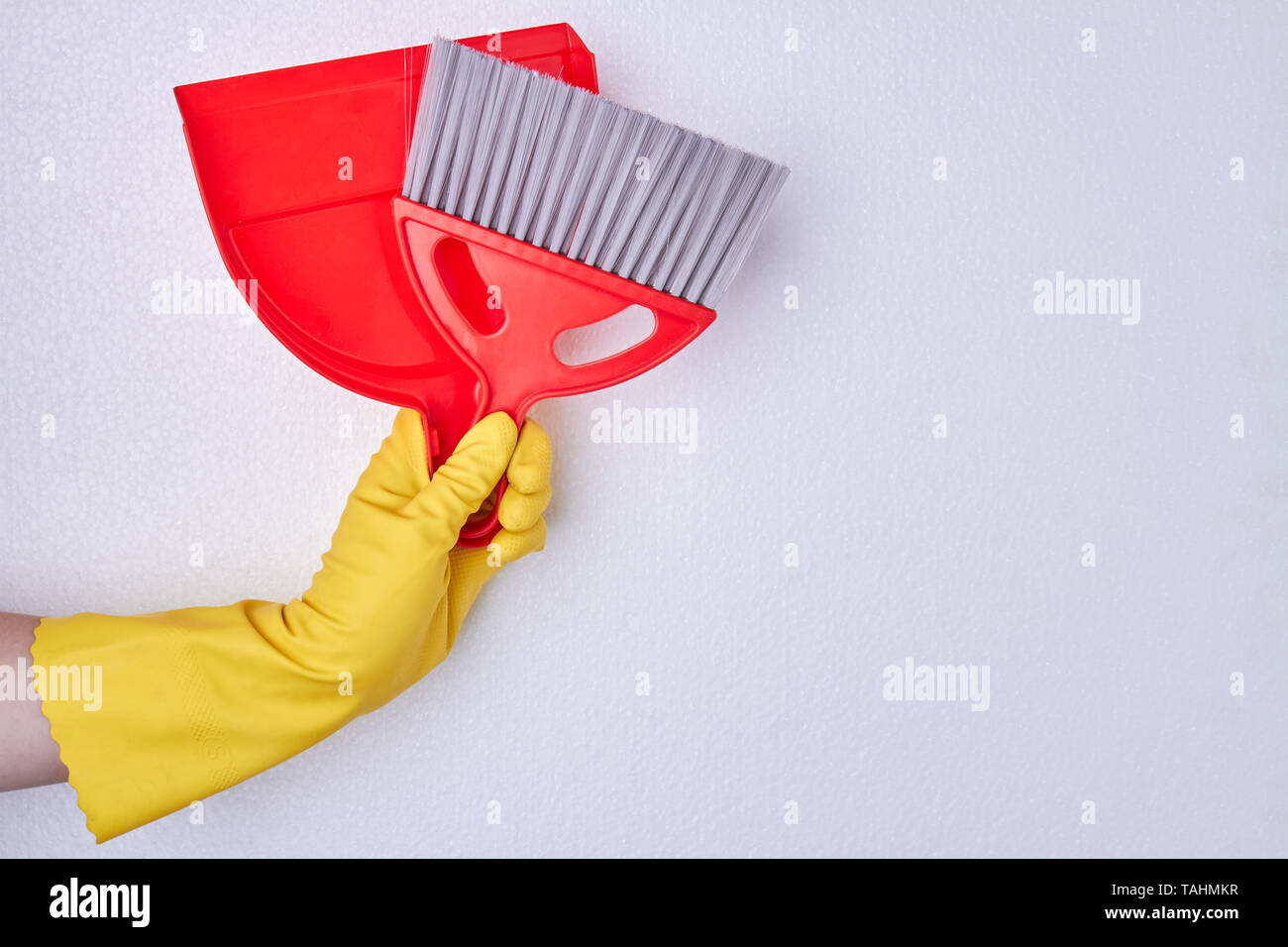 Hand in gloves holding dustpan and brush. Concept of cleaning service. Stock Photo