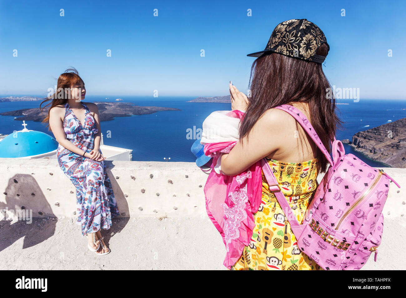 Two young Asian women tourists taking photo with phone, fashion backpack brand MCM, Santorini Greek Islands Greece, Europe travelling people Stock Photo