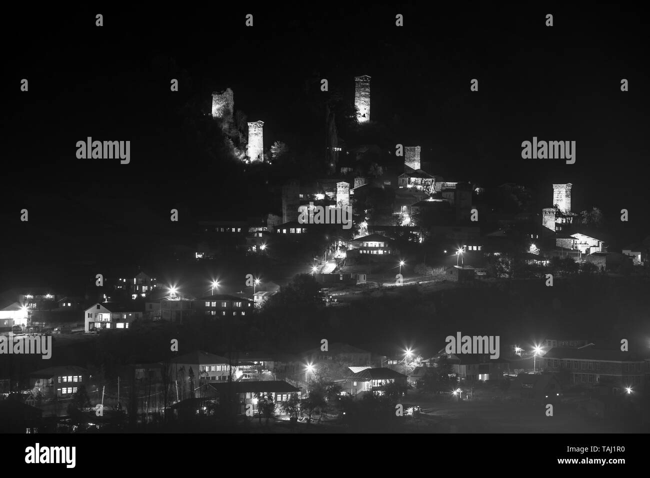 View of Svan towers with night illumination in Mestia village at night. Upper Svaneti, Georgia. Black and white Stock Photo