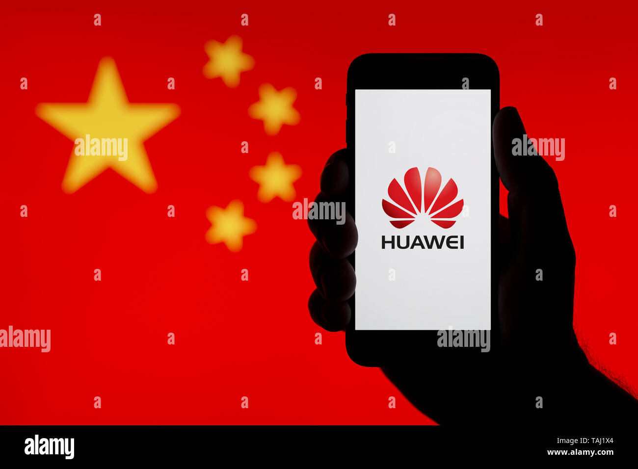 A silhouetted hand of a man holds a smartphone displaying the logo of Chinese company Huawei, with a China flag in the background (Editorial use only) Stock Photo